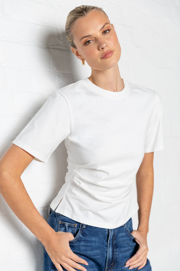 Woman wearing a white t-shirt with side ruching and blue jeans against a plain background