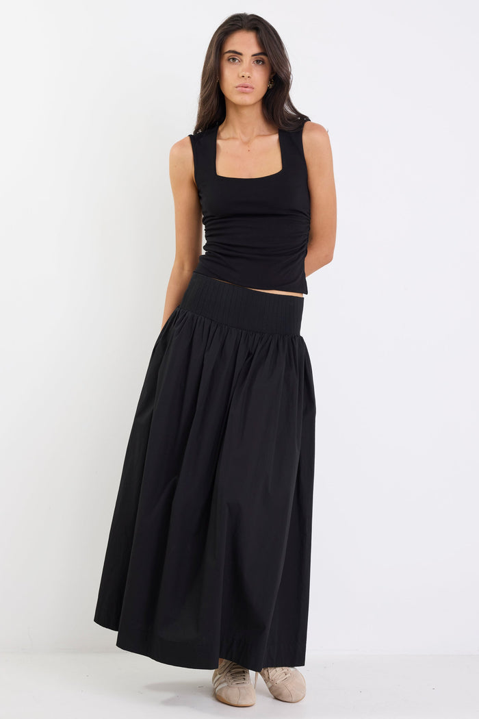 Woman wearing a black sleeveless top and long black skirt on a white background