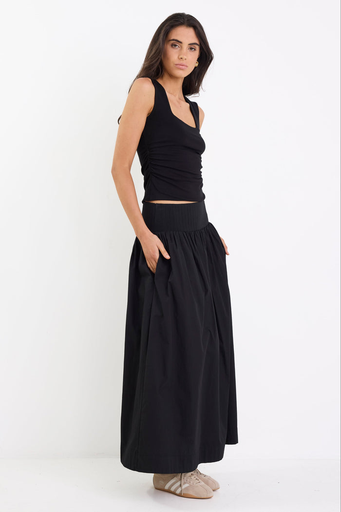 Woman wearing a black sleeveless top and long black skirt on a white background