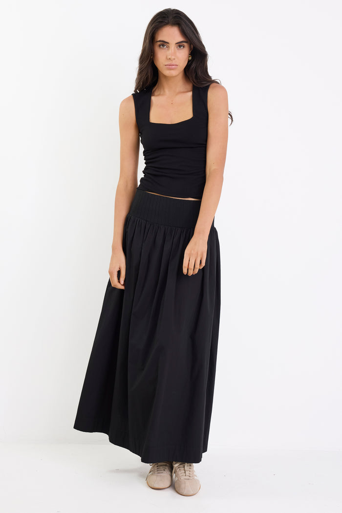Woman wearing a black sleeveless top and long skirt on a white background