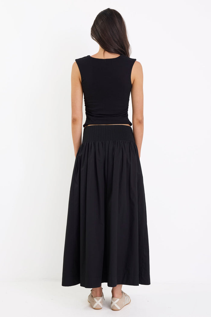 Woman wearing a black sleeveless top and long skirt on a white background