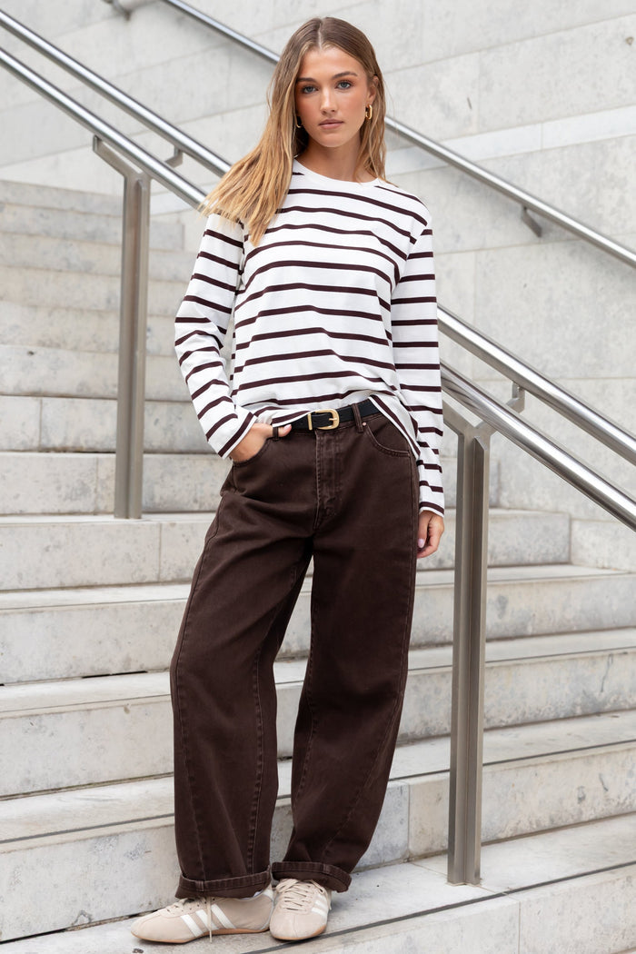 Woman in a striped sweater and brown pants standing on a staircase.