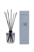 A reed diffuser bottle with black reeds next to its light blue packaging box. The box is branded 'The Powder Room' and 'AB All Purpose Room'.