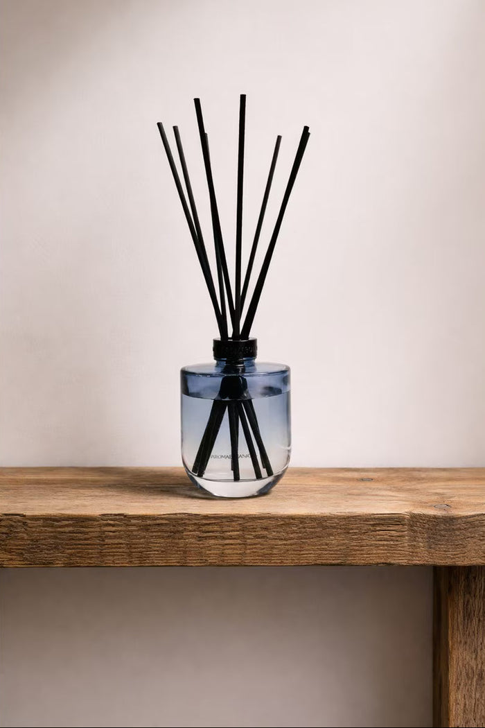 Glass diffuser with black sticks on a wooden surface against a plain background