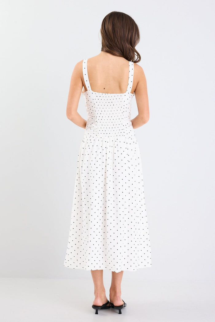 Woman wearing a white dress with black polka dots on a plain background