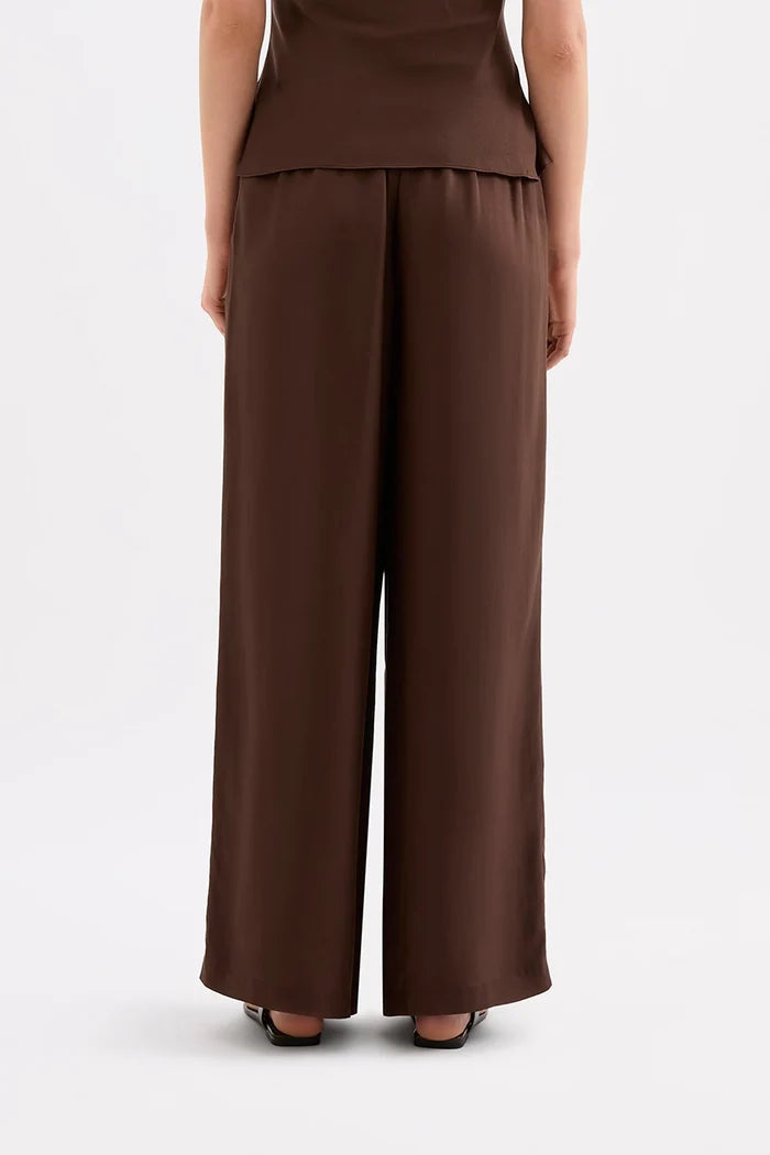 A model shown from the back wearing brown wide-leg trousers and a matching brown top, standing against a light gray studio background.