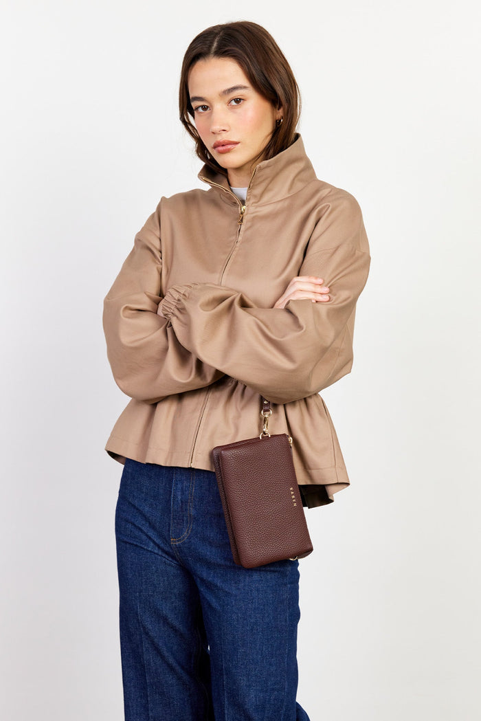 Woman wearing a beige jacket and blue jeans, holding a brown leather bag on a white background