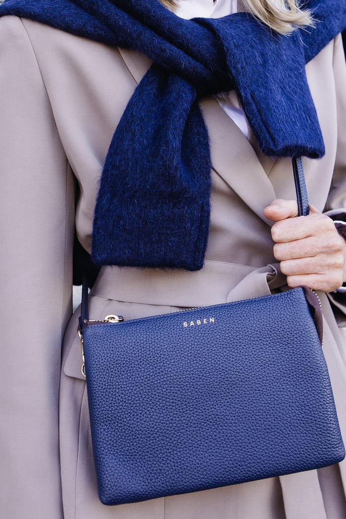 Person wearing a blue scarf and holding a blue handbag with a visible brand logo.