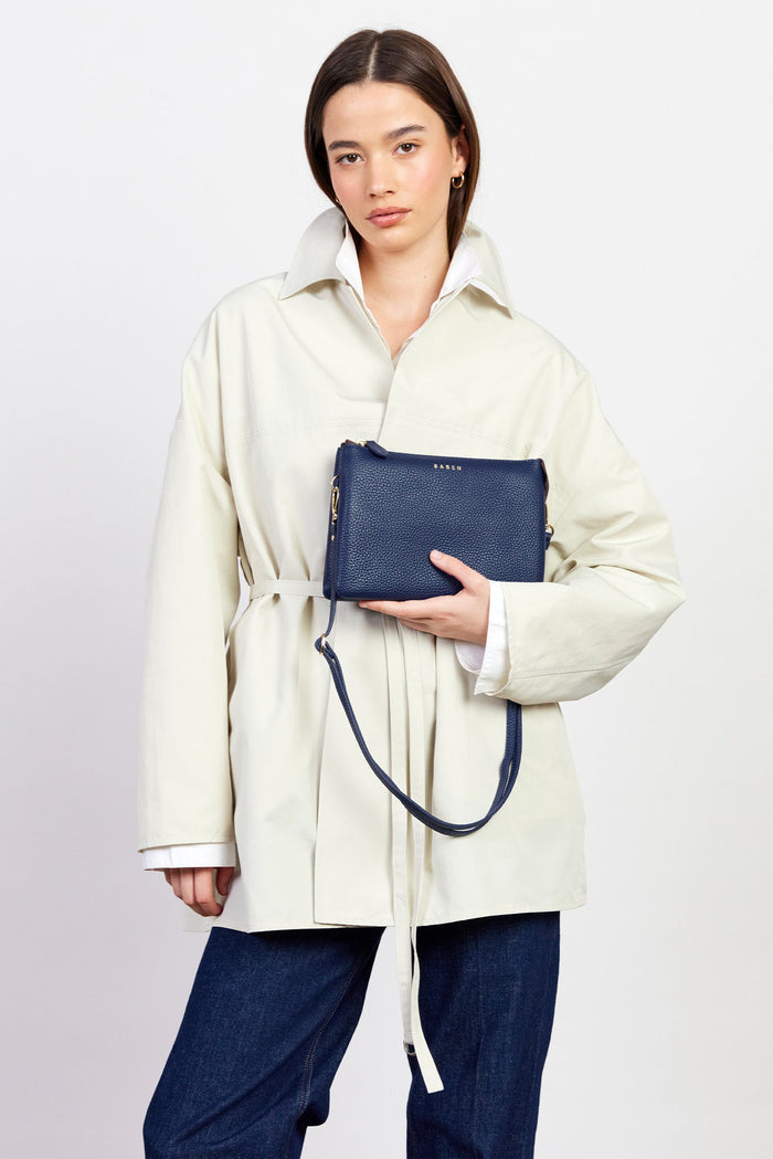 Person wearing a cream coat holding a navy blue bag against a white background