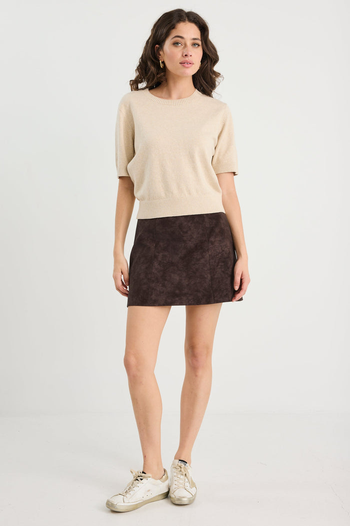 Woman wearing a beige sweater and brown skirt on a white background