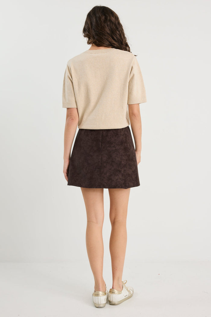 Person wearing a beige top and brown skirt on a white background