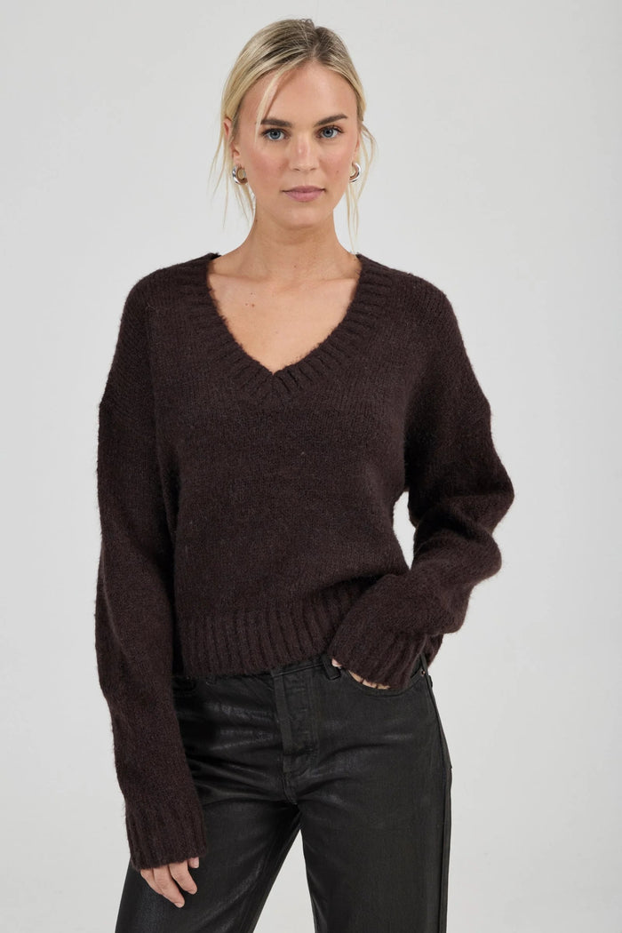 Woman wearing a brown sweater and black pants against a plain background