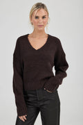 Woman wearing a brown sweater and black pants against a plain background