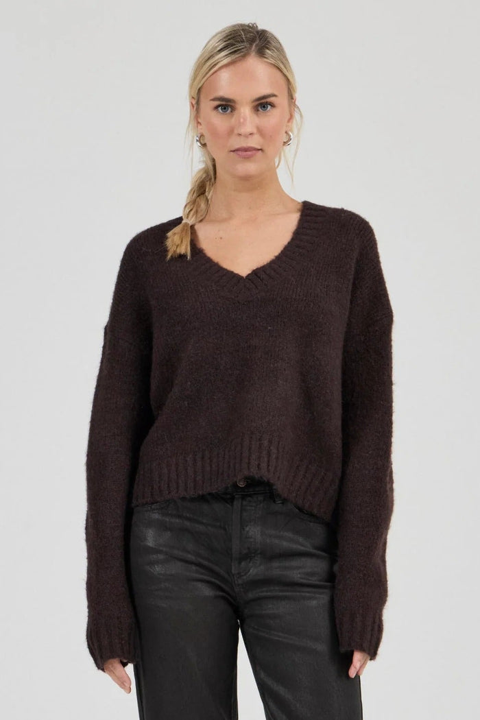 Woman wearing a brown sweater and black pants on a white background