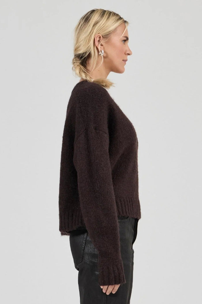 Woman wearing a brown sweater and black pants on a white background