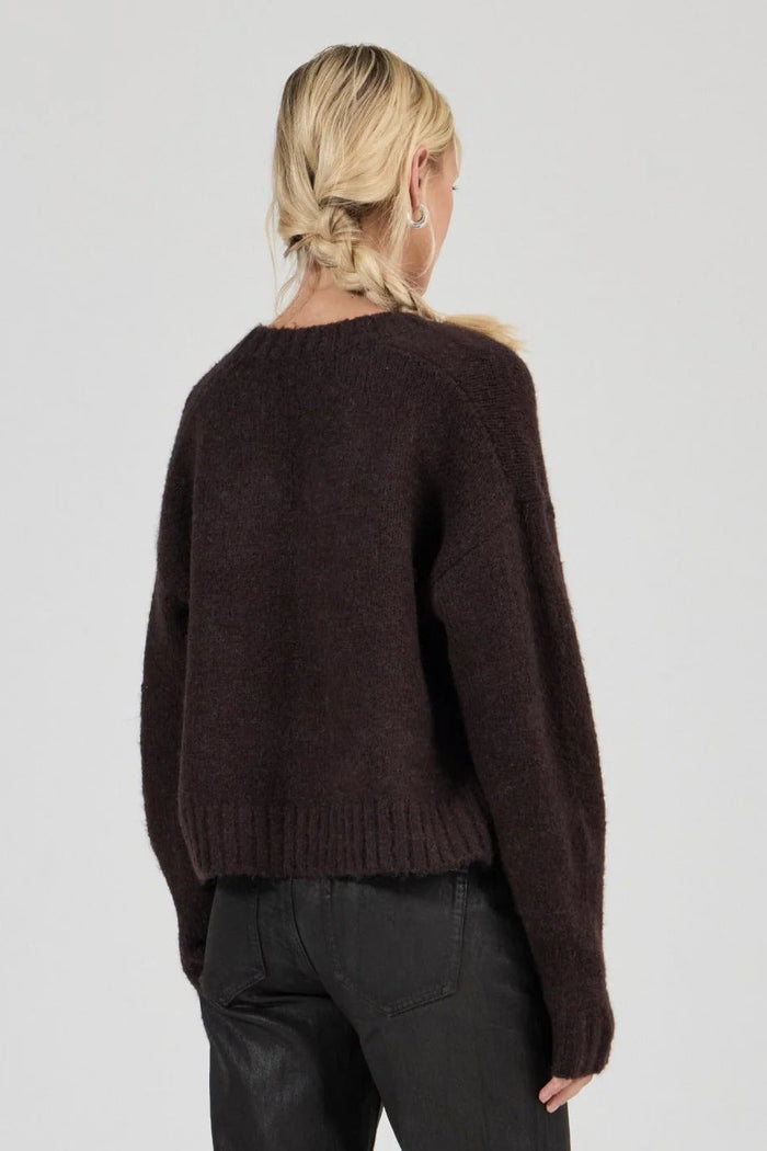 Person wearing a brown sweater and black pants on a white background