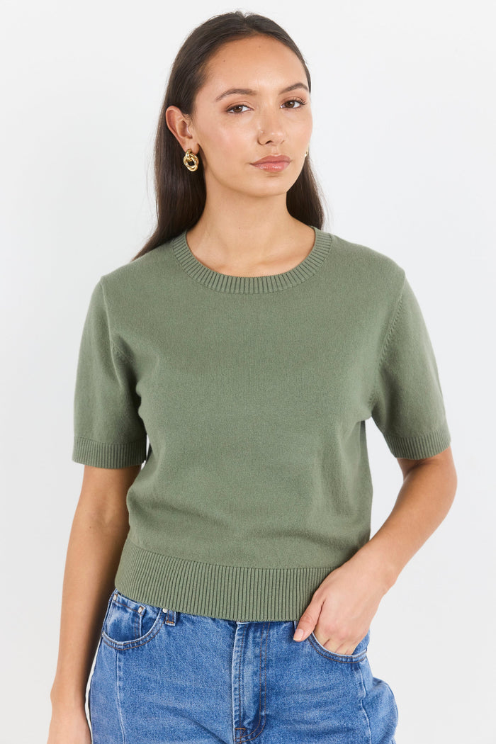 Woman wearing a green sweater and blue jeans against a white background