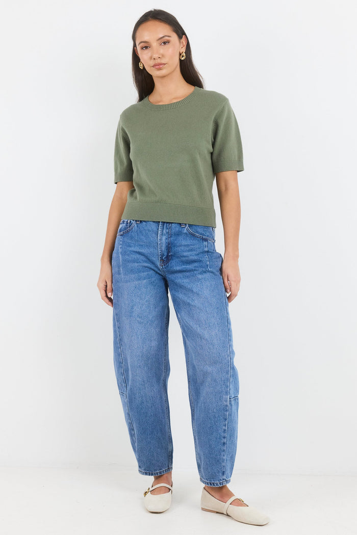 Woman wearing a green sweater and blue jeans on a white background