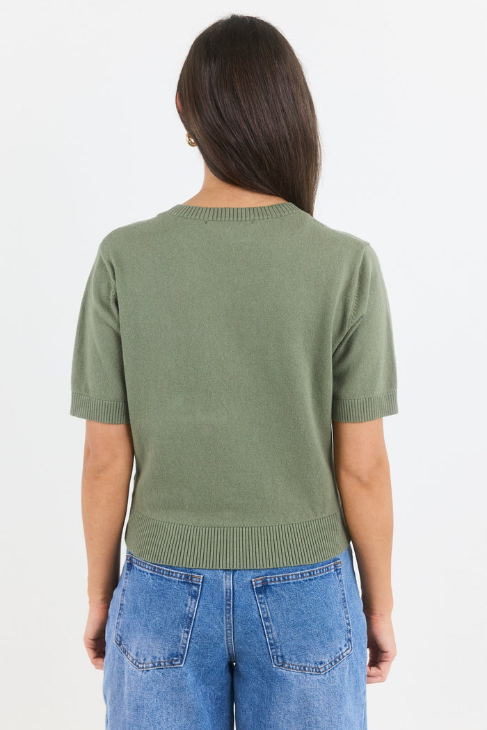 Person wearing a green sweater and blue jeans on a white background