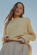 Woman wearing a yellow sweater and beige pants against a clear blue sky.