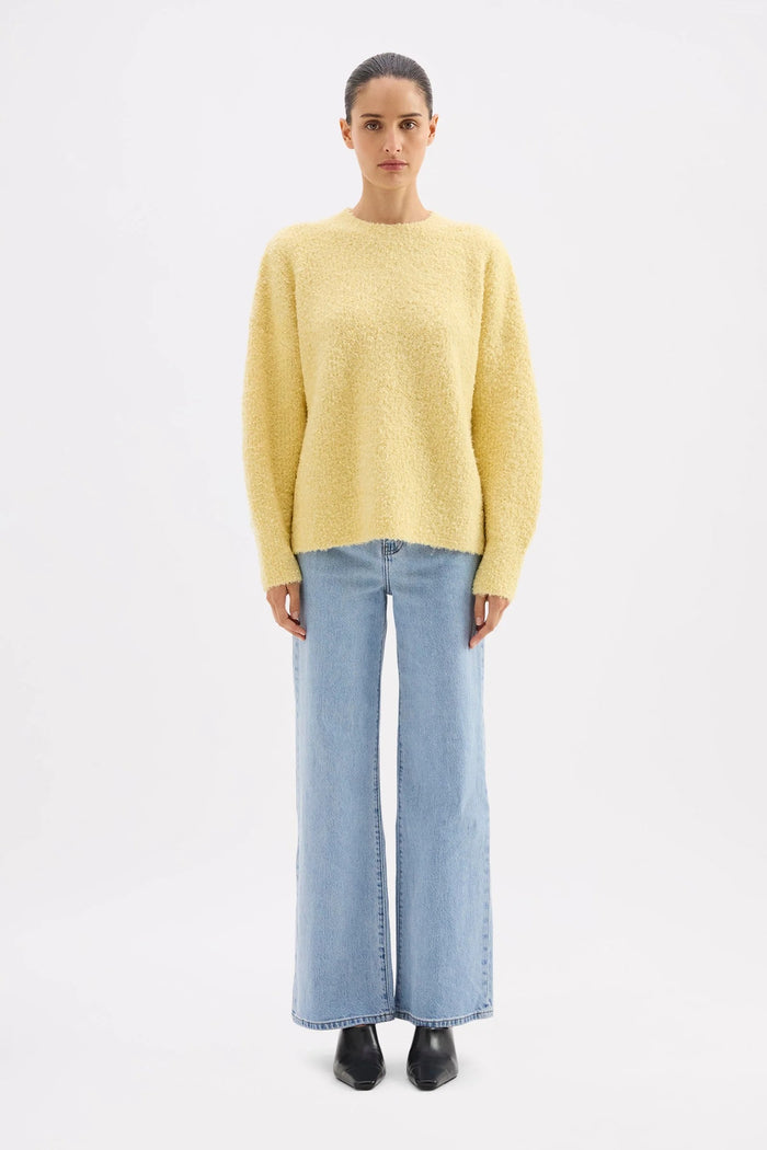 Person wearing a yellow sweater and light blue jeans on a white background