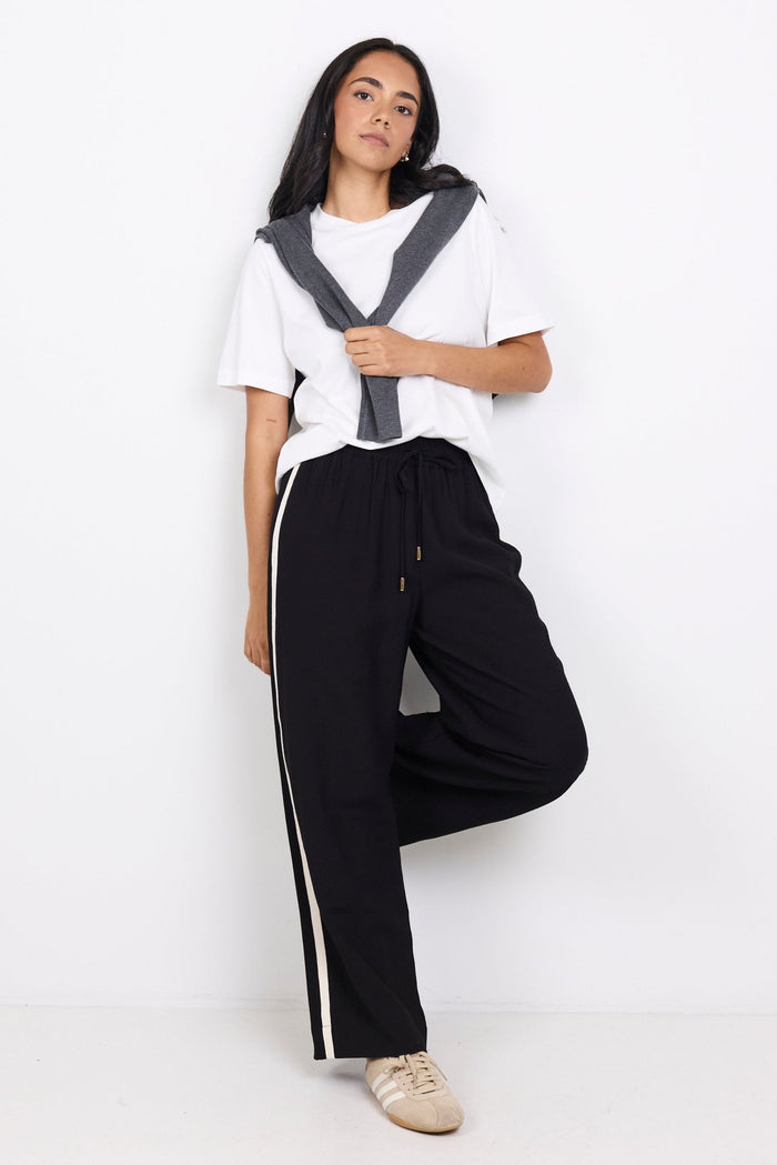 Person wearing a white shirt with a black vest and black pants with white stripes on a white background