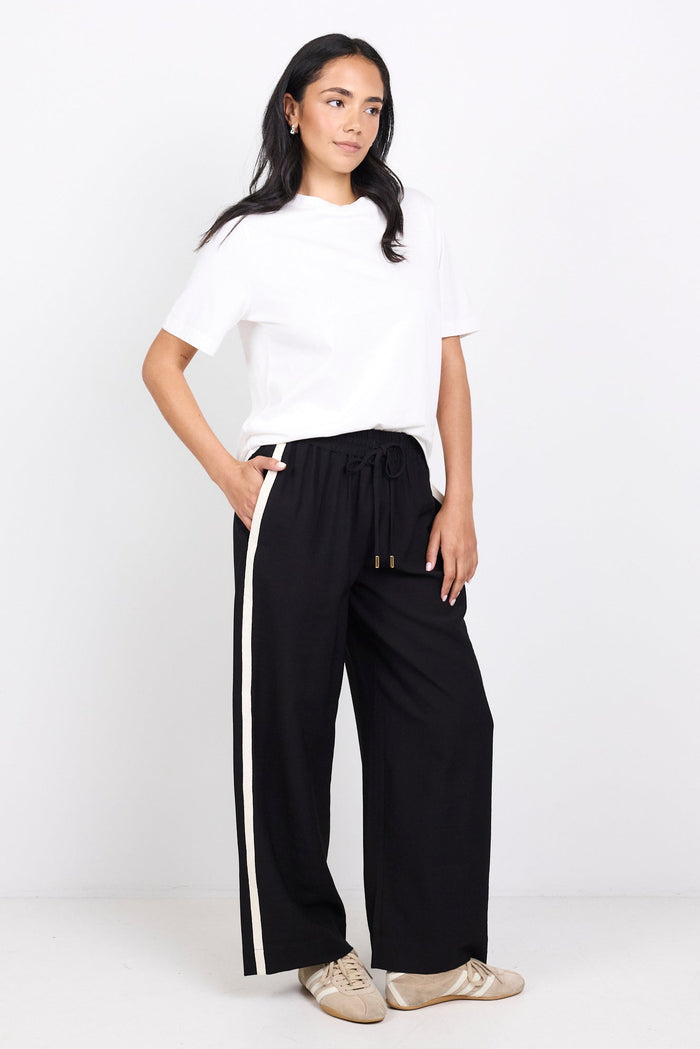 Woman wearing a white top and black pants with white stripes on a white background