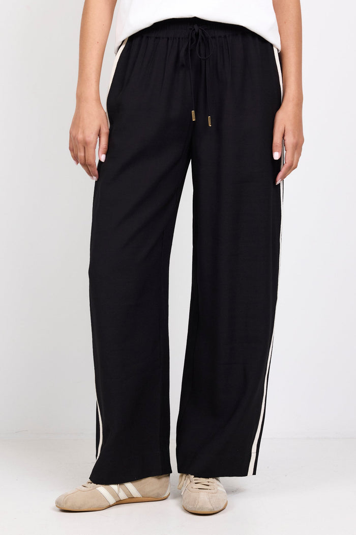 Person wearing black wide-leg pants with white stripes on a white background