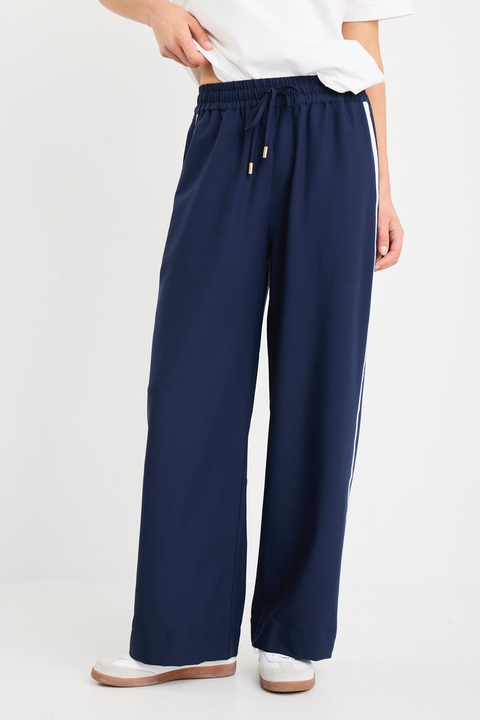 Woman wearing high-rise plain navy wide-leg pants with an elastic waistband and drawstring tie, styled with white sneakers and a white tee.