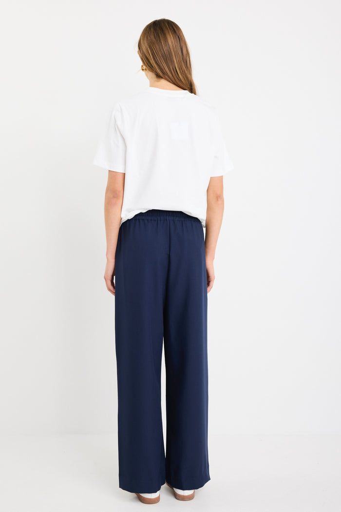 Woman wearing high-rise plain navy wide-leg pants with an elastic waistband and drawstring tie, styled with white sneakers and a white tee.