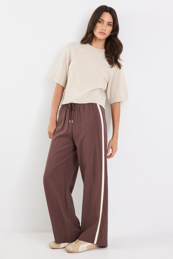 Woman wearing a beige top and brown pants with a white stripe on a white background