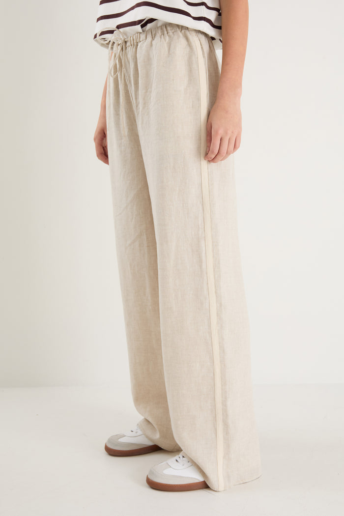 Woman in beige linen pants with side stripe detail and an elastic waistband, paired with a white stripe top.