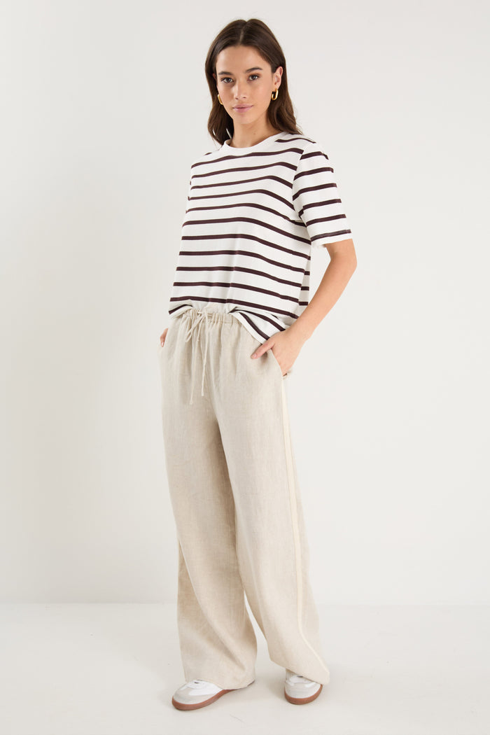 Woman in beige linen pants with side stripe detail and an elastic waistband, paired with a white stripe top.