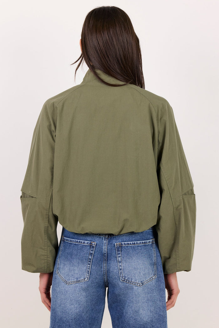 A model shown from the back wearing an olive green utility-style jacket and blue jeans against a plain off-white studio background.
