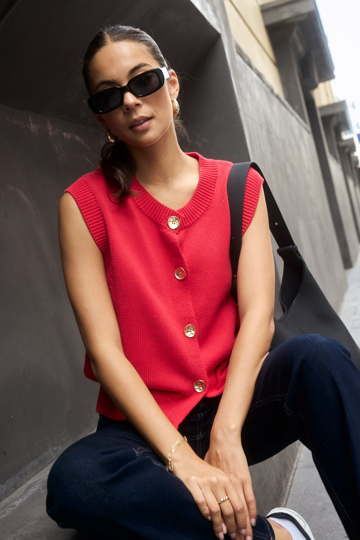 Model wears a cherry red knit vest with gold buttons.