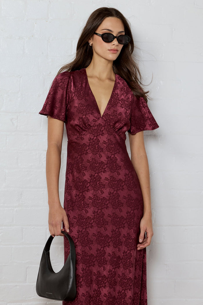 Woman wearing a burgundy patterned dress against a white brick wall