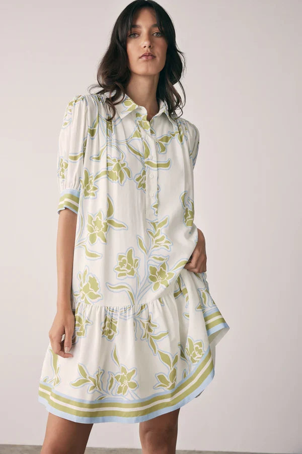 Woman wearing a white dress with green floral pattern against a plain background