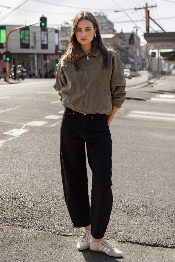 Woman standing on a city street wearing a gray sweater and black pants.
