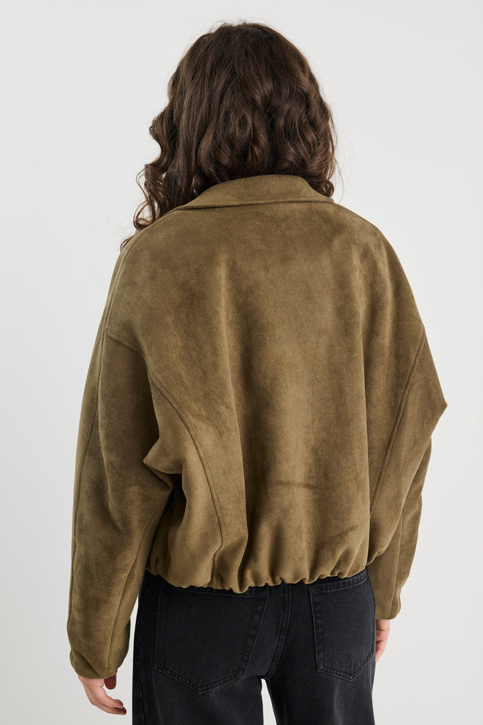Woman wearing a khaki mock suede zip-up jacket with a soft, textured finish and a relaxed fit, styled over a beige knit top and black jeans.
col_pattern