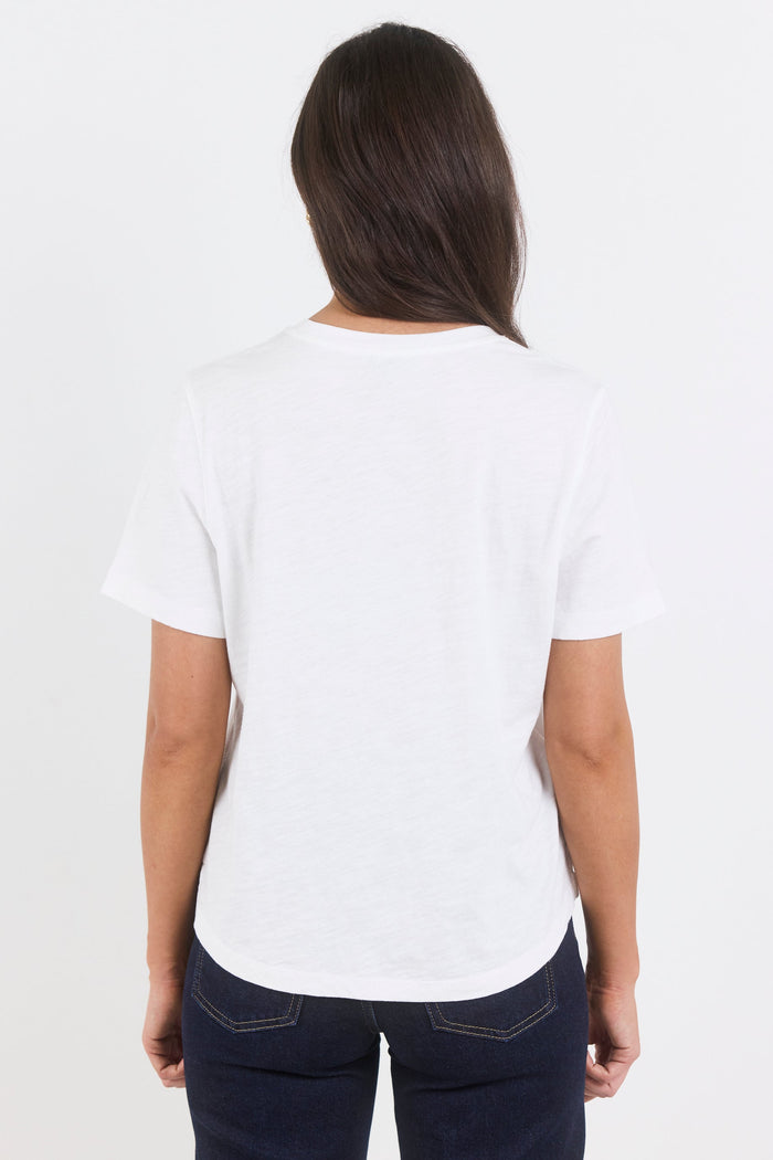 A woman viewed from behind wearing a plain white short-sleeve crewneck t-shirt and dark navy blue jeans against a light gray studio background.