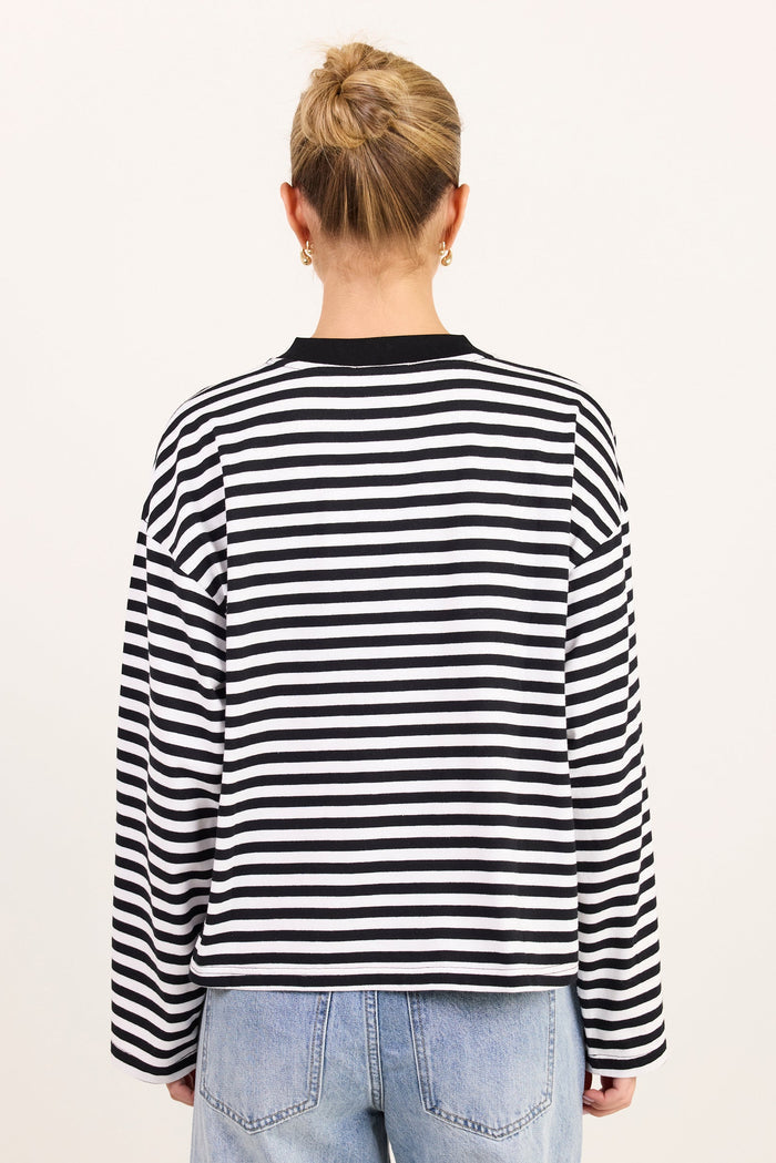 A person viewed from the back wearing a black and white horizontally striped long-sleeve top with a black crew neck, paired with light blue jeans, against a plain off-white background.