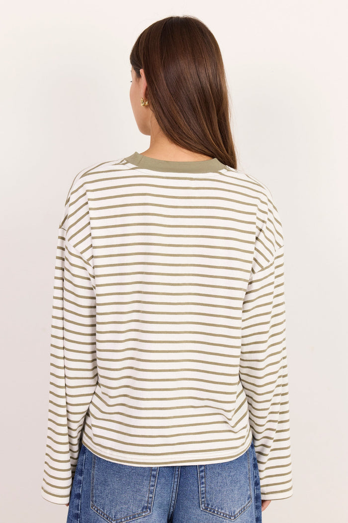A woman viewed from the back wearing a cream and olive green horizontally striped long-sleeve top with blue jeans, set against a plain off-white background.