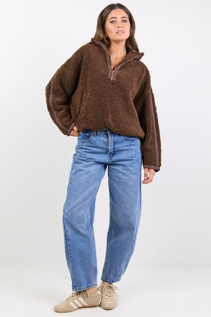 Person wearing a brown fleece pullover and blue jeans on a white background