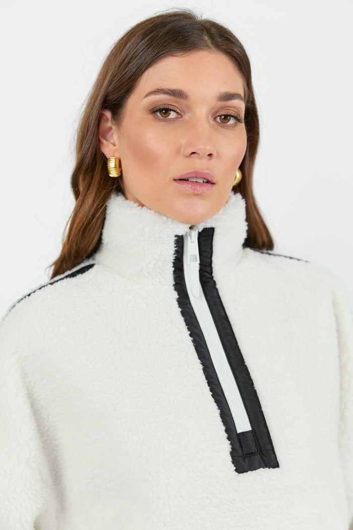 This cozy cream fleece jacket features a zip-up front, sporty black side stripes, and a relaxed fit, paired with black wash jeans for a casual yet stylish look.