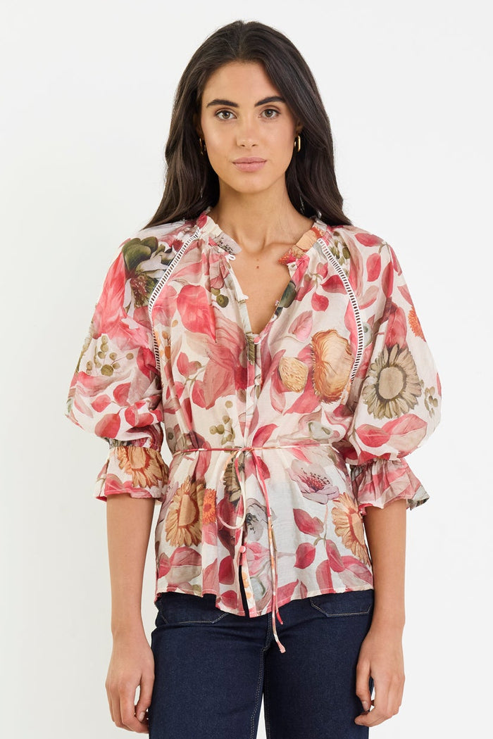 Woman wearing a floral blouse and dark jeans on a white background