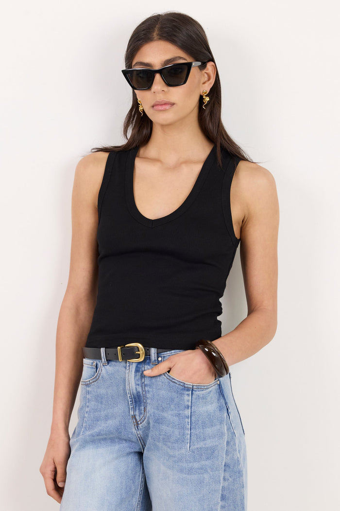 A woman modeling a black ribbed tank top and light-wash blue jeans against a plain white background.