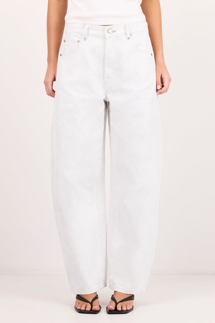 A person wearing white wide-leg jeans with a white top and black sandals, standing against a plain light background.