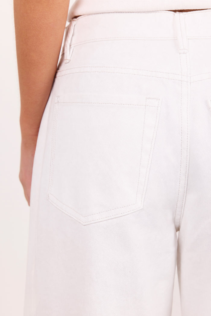 Close-up of the back waistband and pocket area of light-colored pants worn by a model, showing part of the arm and torso against a plain light background.
col_pattern
