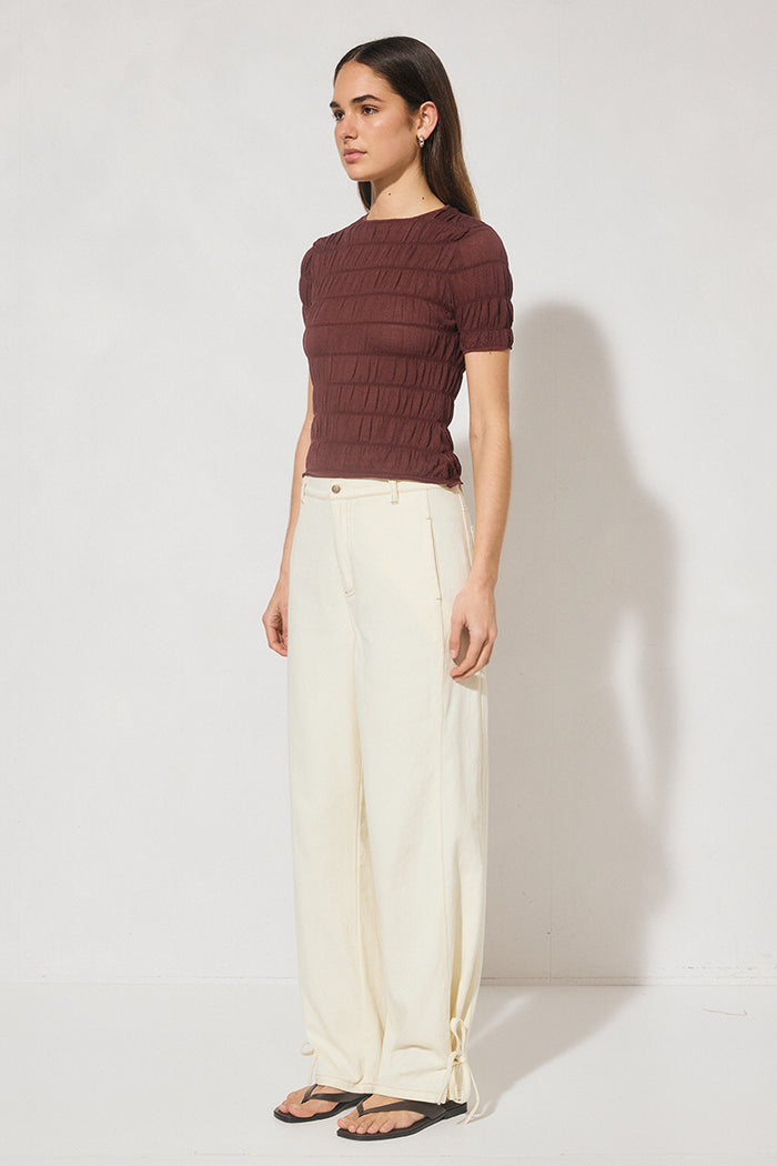 Woman wearing a maroon ribbed sweater and white pants against a white background