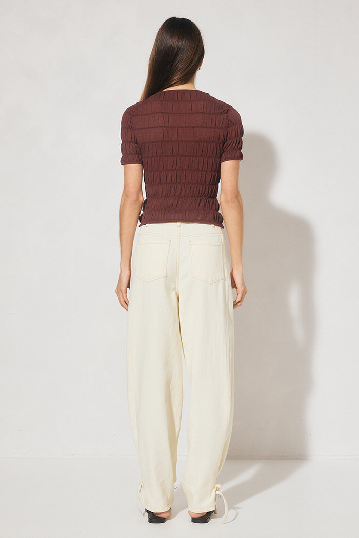 Person wearing a brown ribbed sweater and white pants against a white background